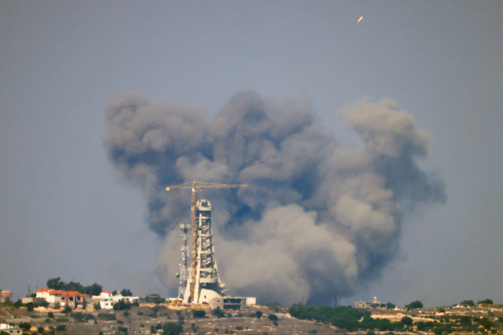 Smoke billows over a horizon with a tower and crane in the foreground.