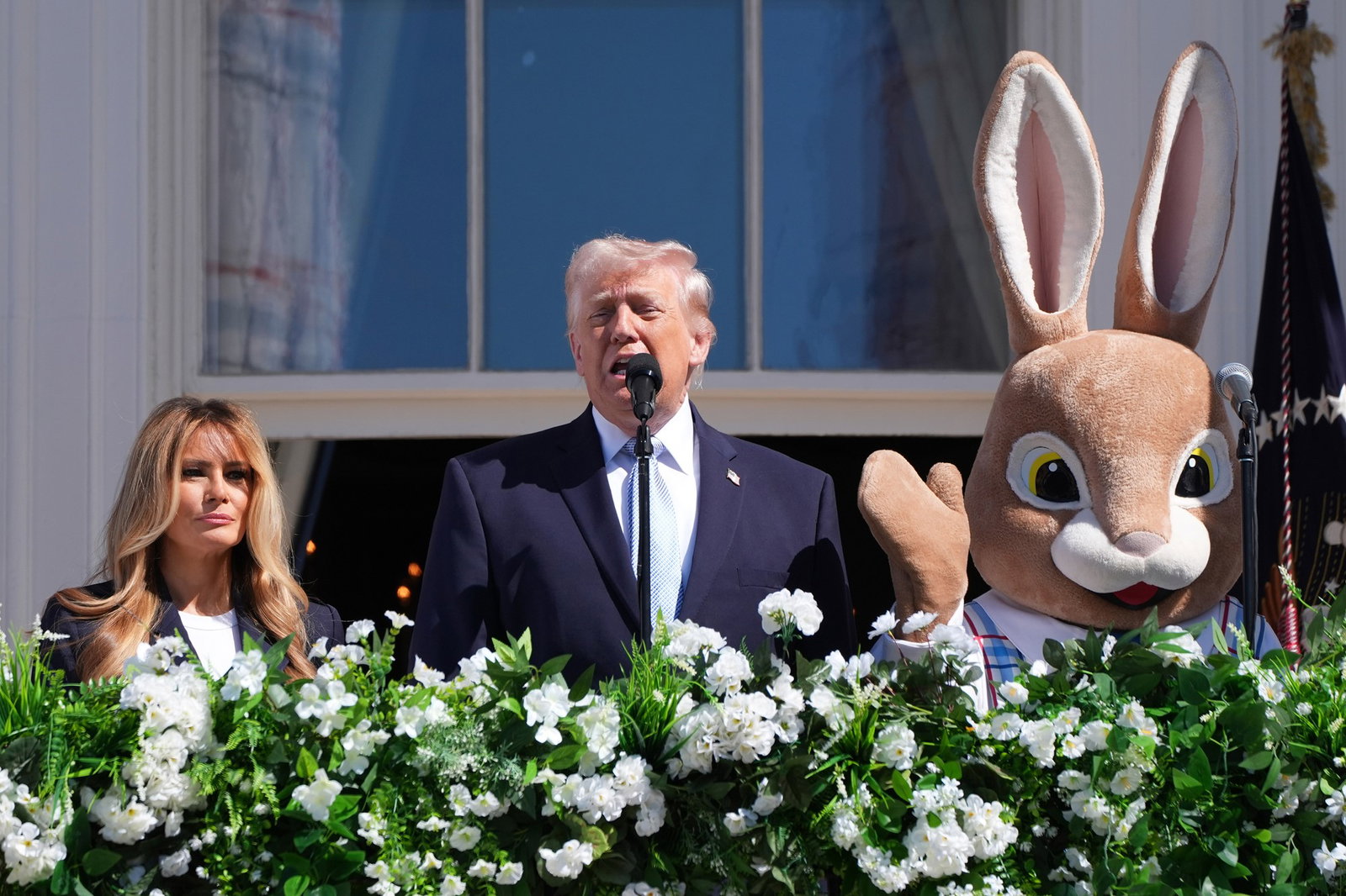 Un hombre habla por un micrófono, a ambos lados hay una mujer y una persona disfrazada de conejito de Pascua.