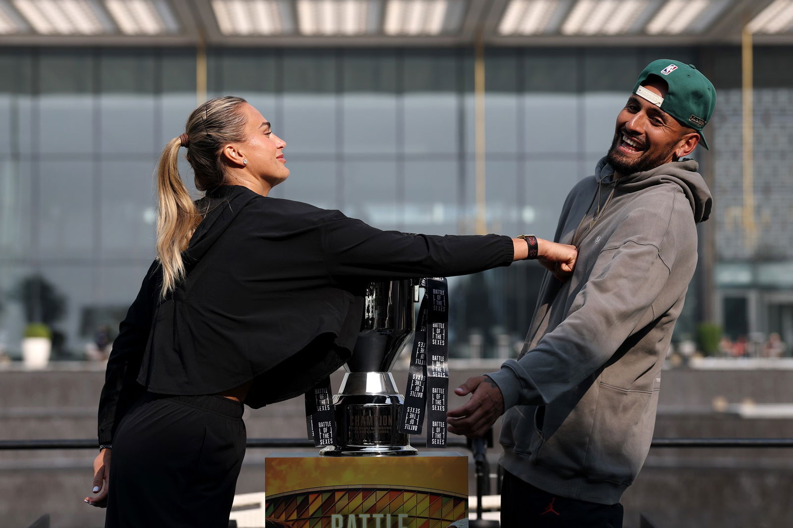 Aryna Sabalenka dá um soco falso em Nick Kyrgios, que ri. Um troféu está entre eles.