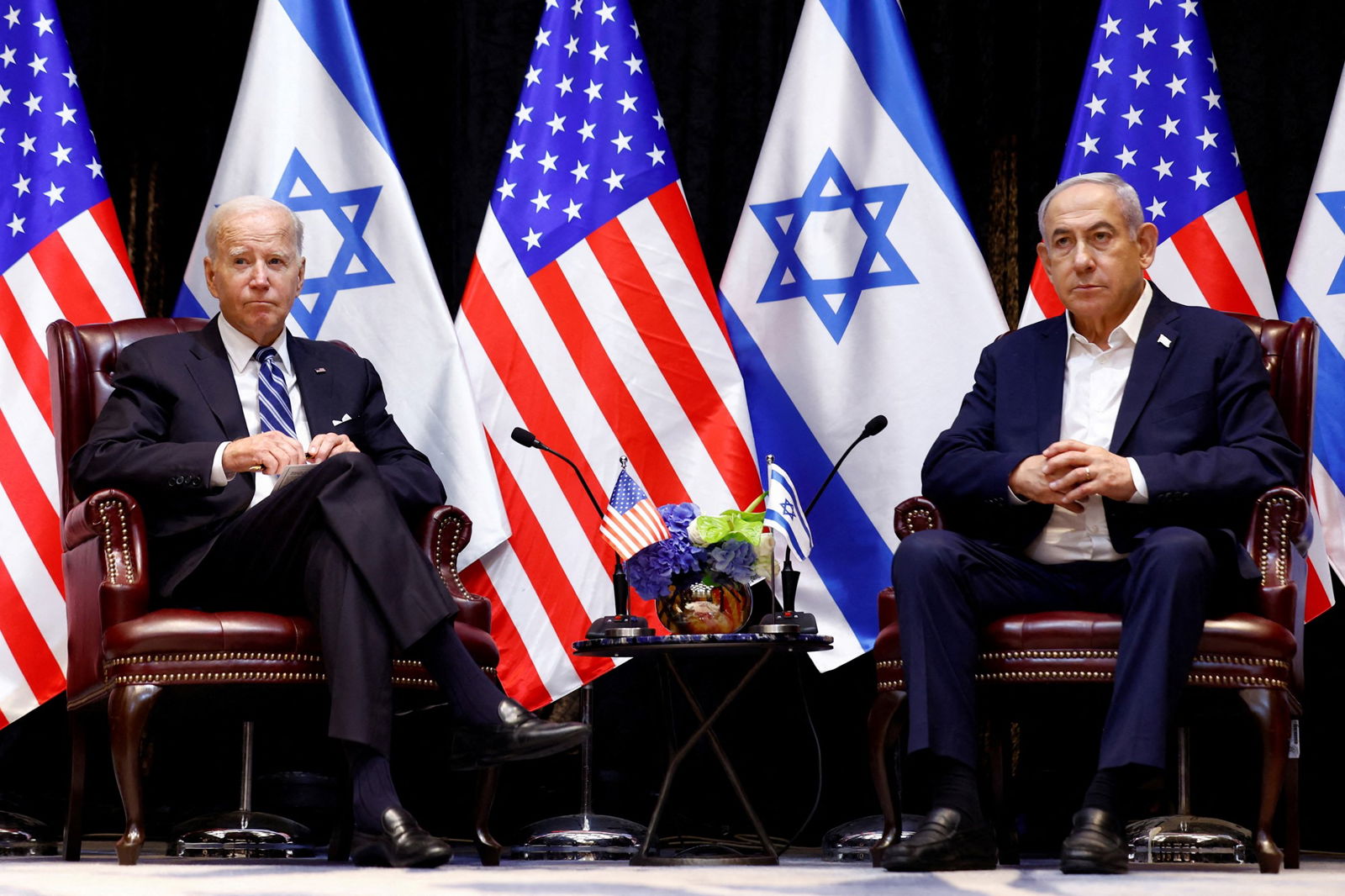 Joe Biden and Benjamin Netanyahu sit on two arm chairs next to each other with Israeli and USA flags behind