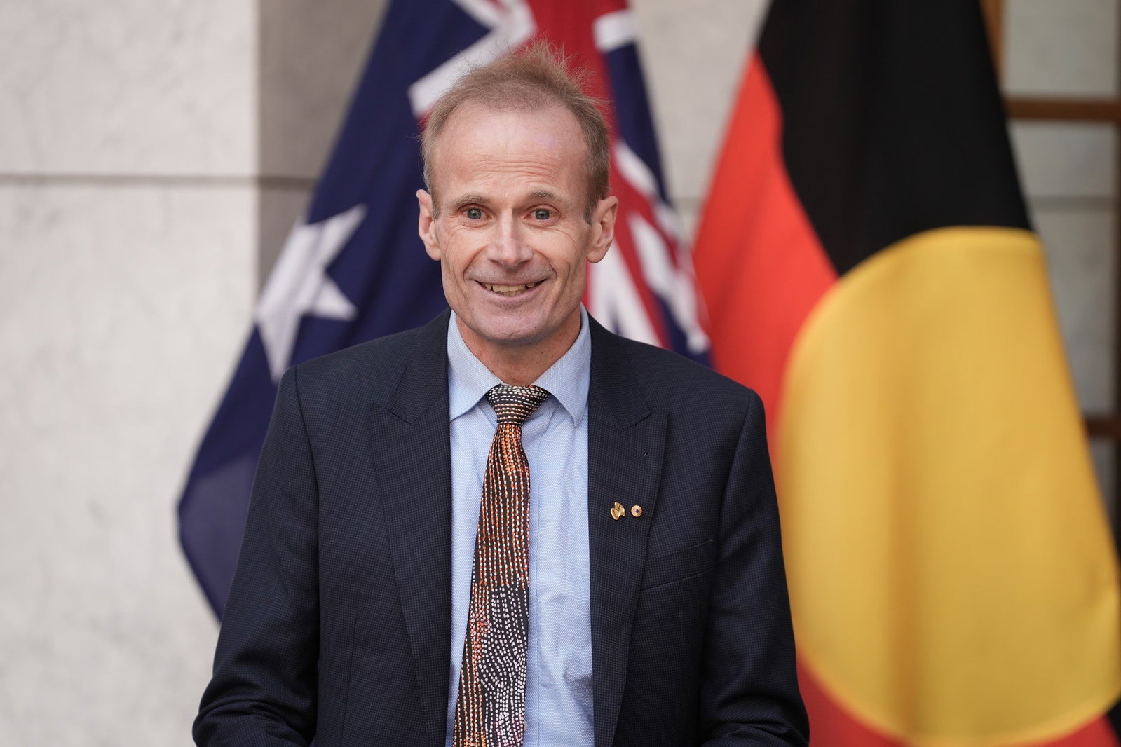 Richard Scolyer smiling with the Australian and Aboriginal flag behind him.