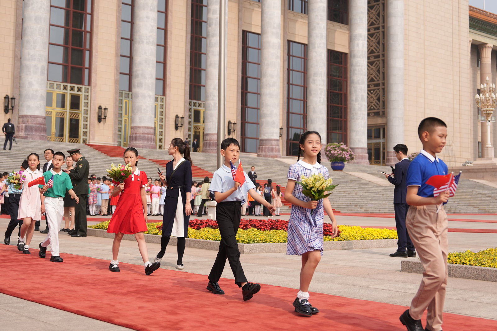 Several children holding flowers walking on a red carpet.