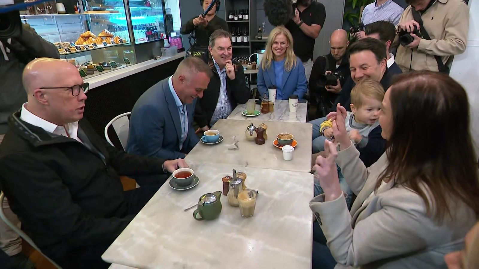 Peter Dutton and Tim Wilson sitting at a cafe table surrounded by men and women