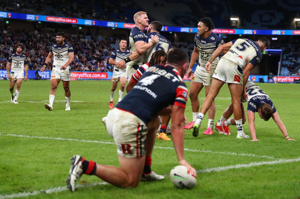 Roosters' Joey Manu kneels as the Cowboys celebrate a try in an NRL game.