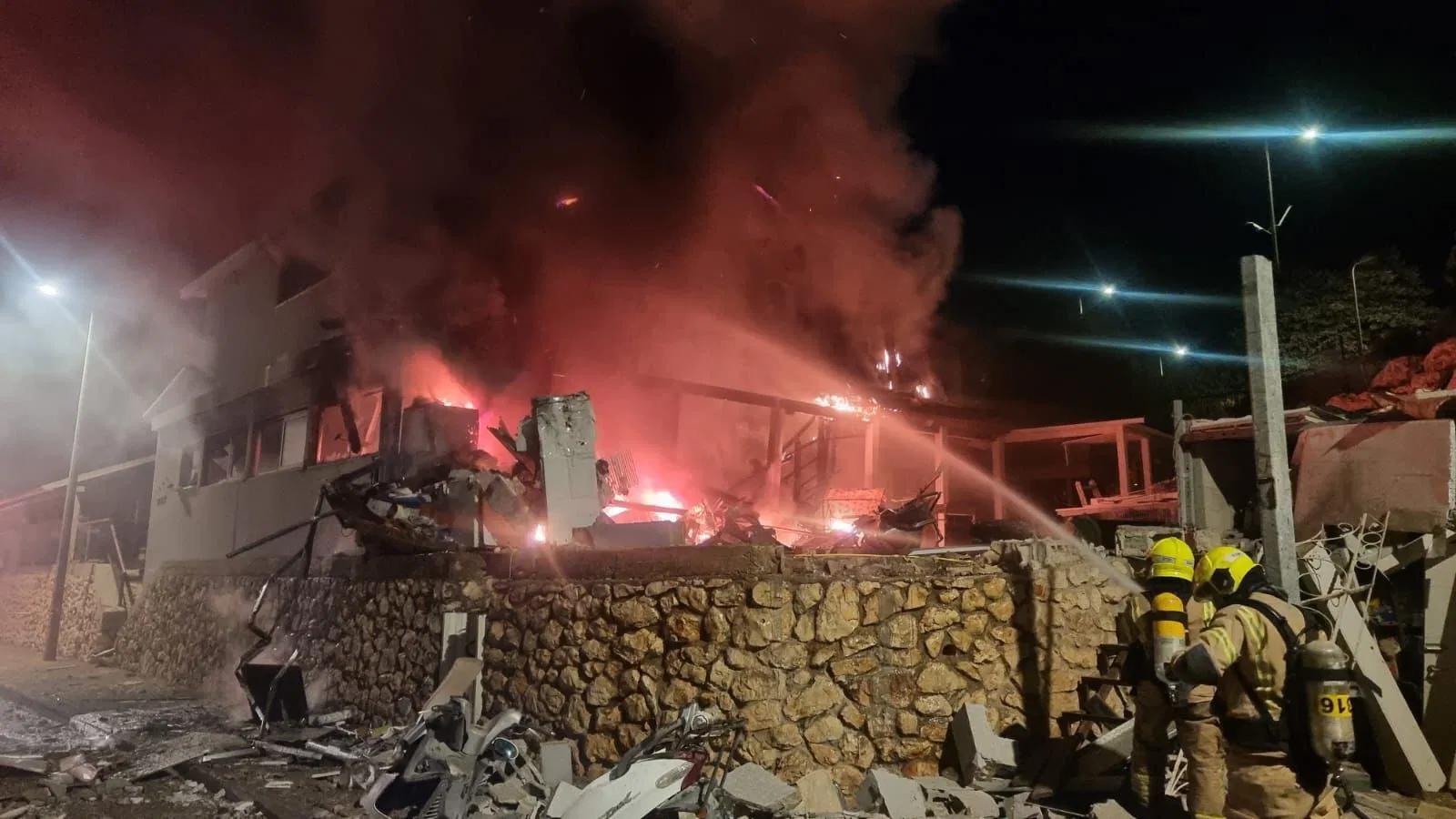 two people spray water on a burning house