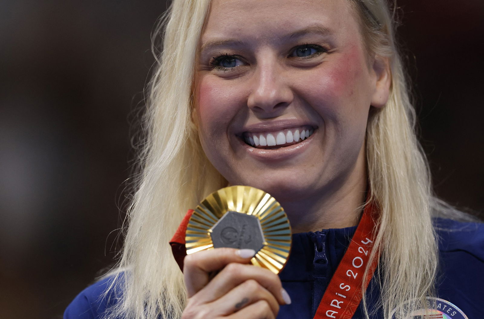 American swimmer Jessica Long holds a gold medal next to her face and has a broad smile.