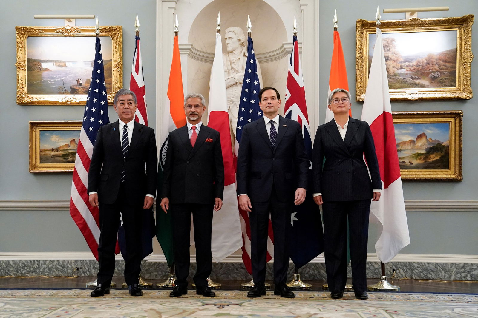 Quad nation representatives, including Marco Rubio and penny Wong, standing in front of flags representing the United States, Japan, India and Australia