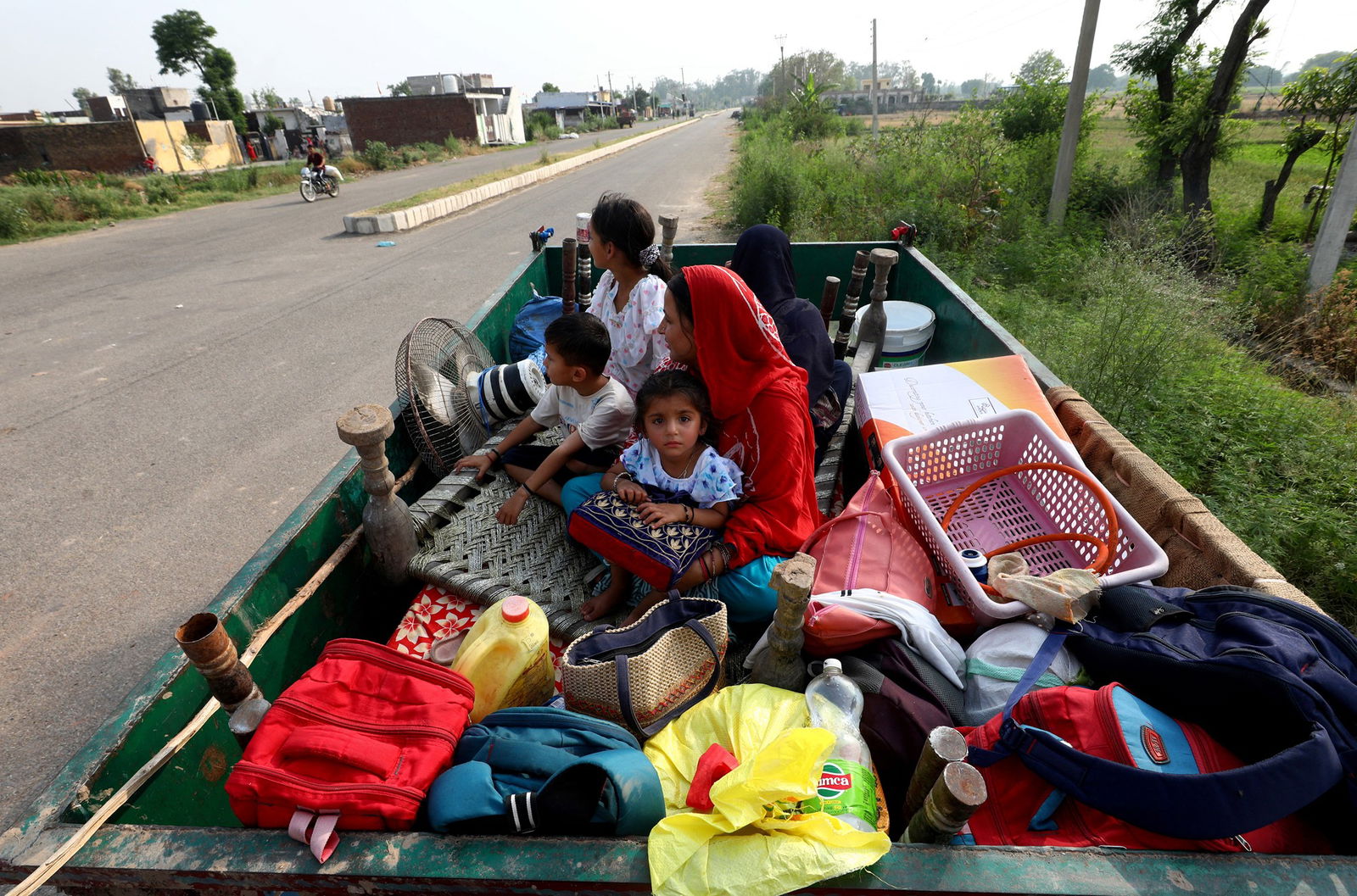 Five people sit in the back of a trailer with home goods strewn all around them