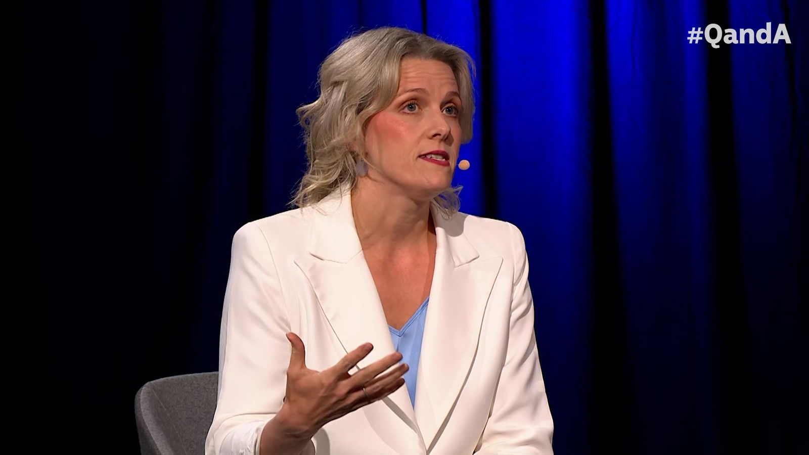 A woman in a white blazer gestures with her hands