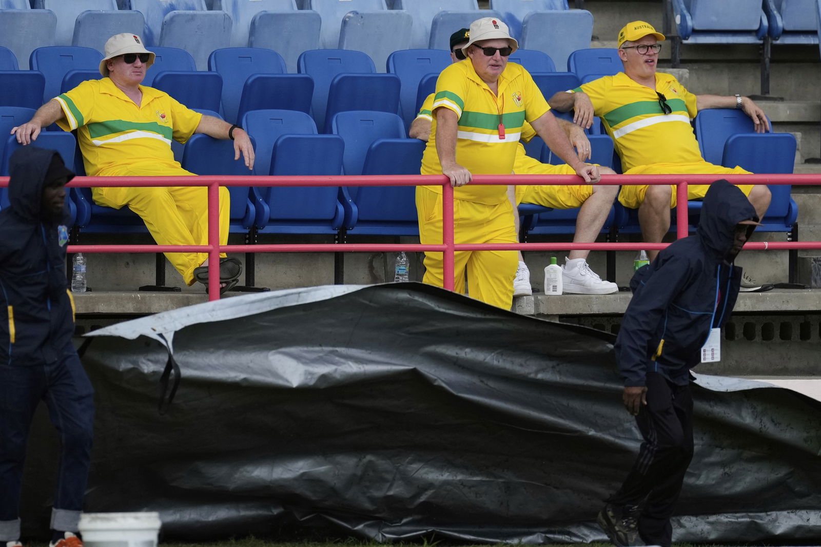 Ground staff run a pitch cover onto the field as Australian supporters look on.