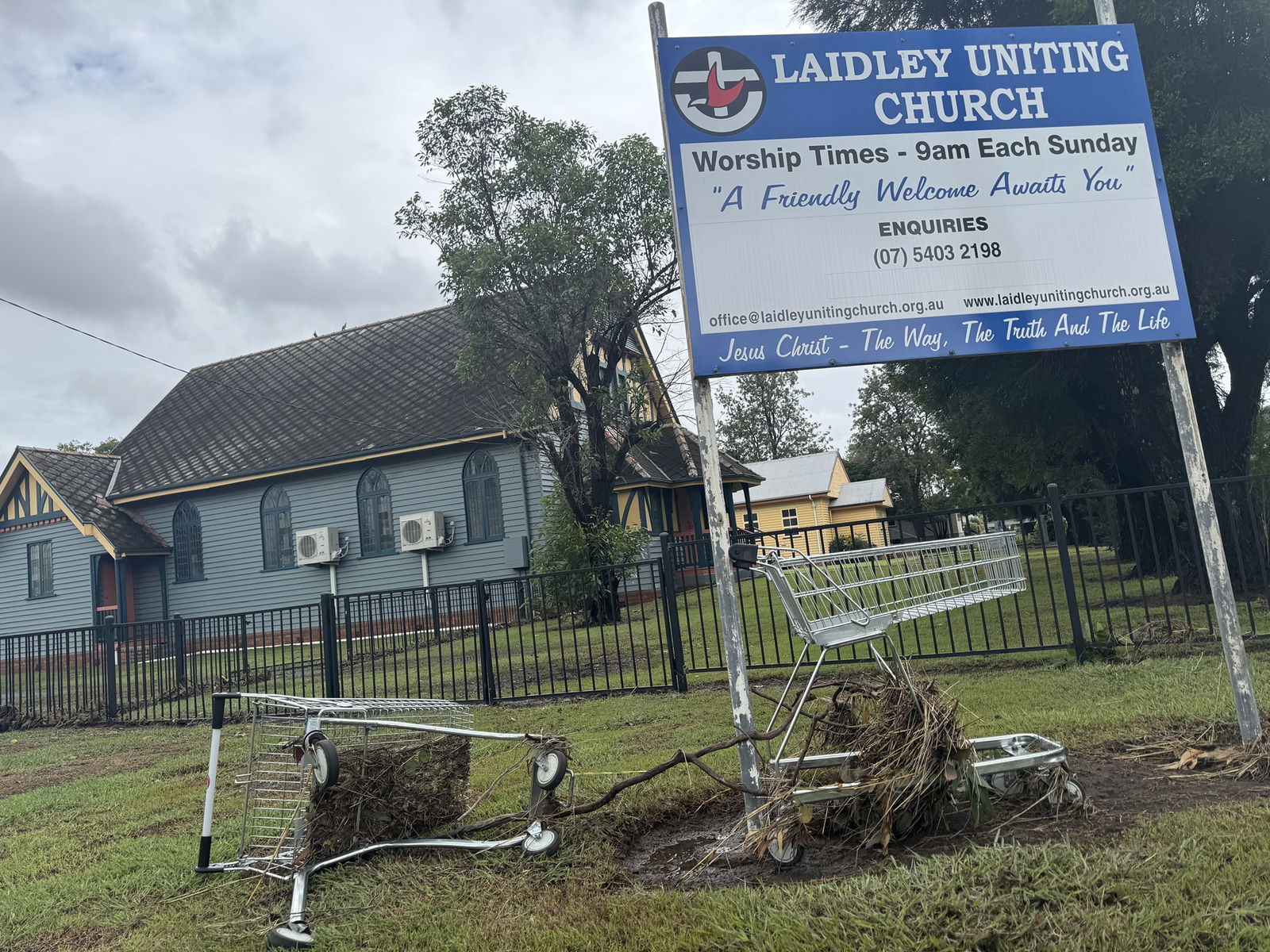 two shopping trolleys washed up in storm water in front of a blue church. 