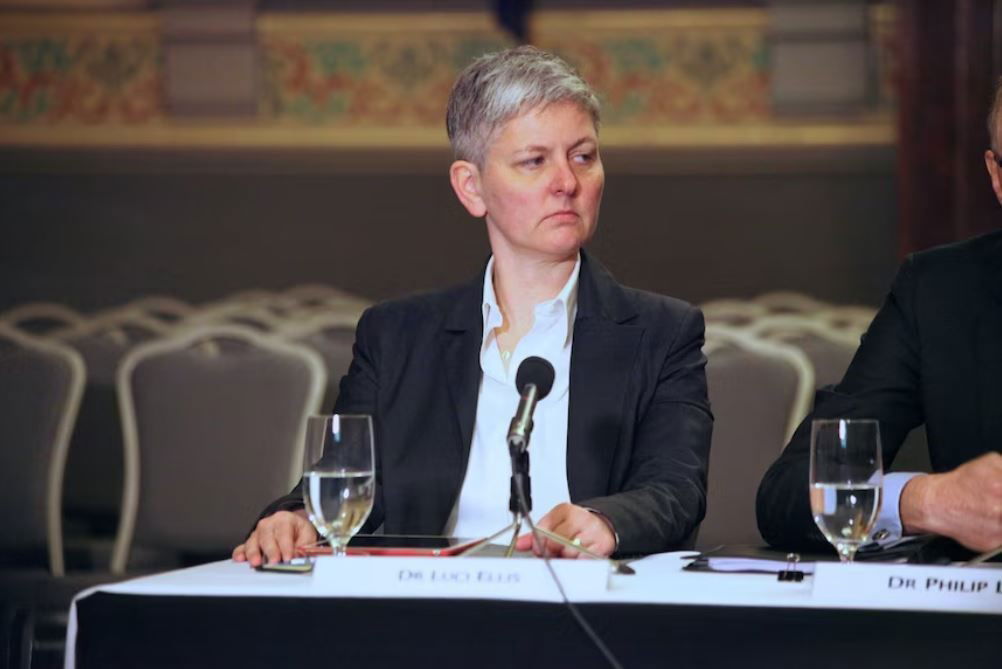 Woman in suit sits before a microphone