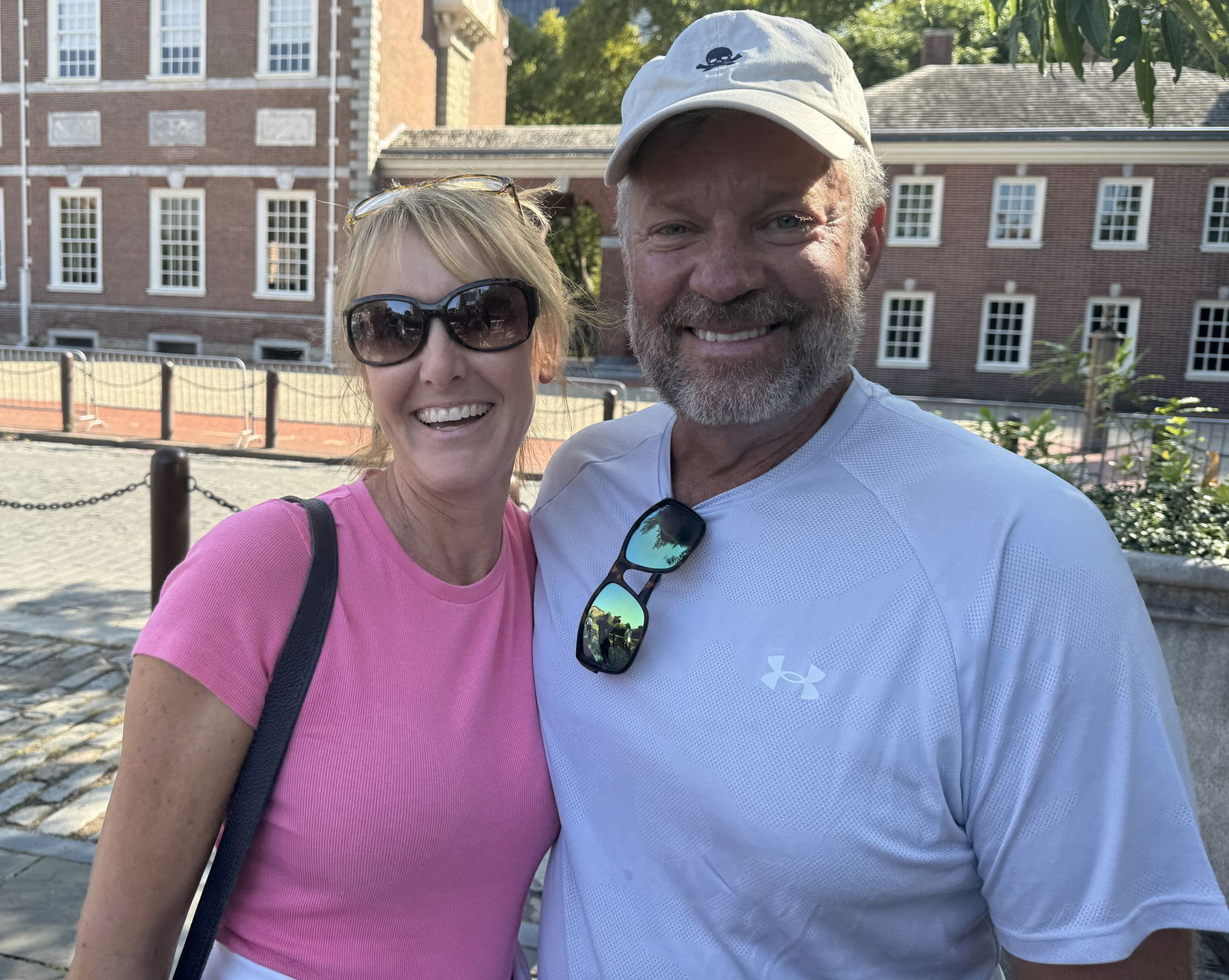 A woman in a pink t-shirt and a man in a white baseball cap pose together for a photo