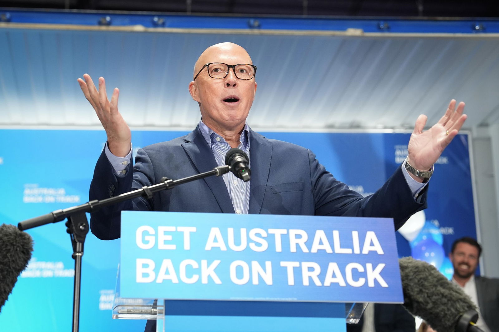 Dutton outstretches his hands as he speaks at a podium