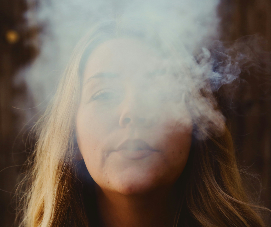 A blonde woman blows smoke into the air.