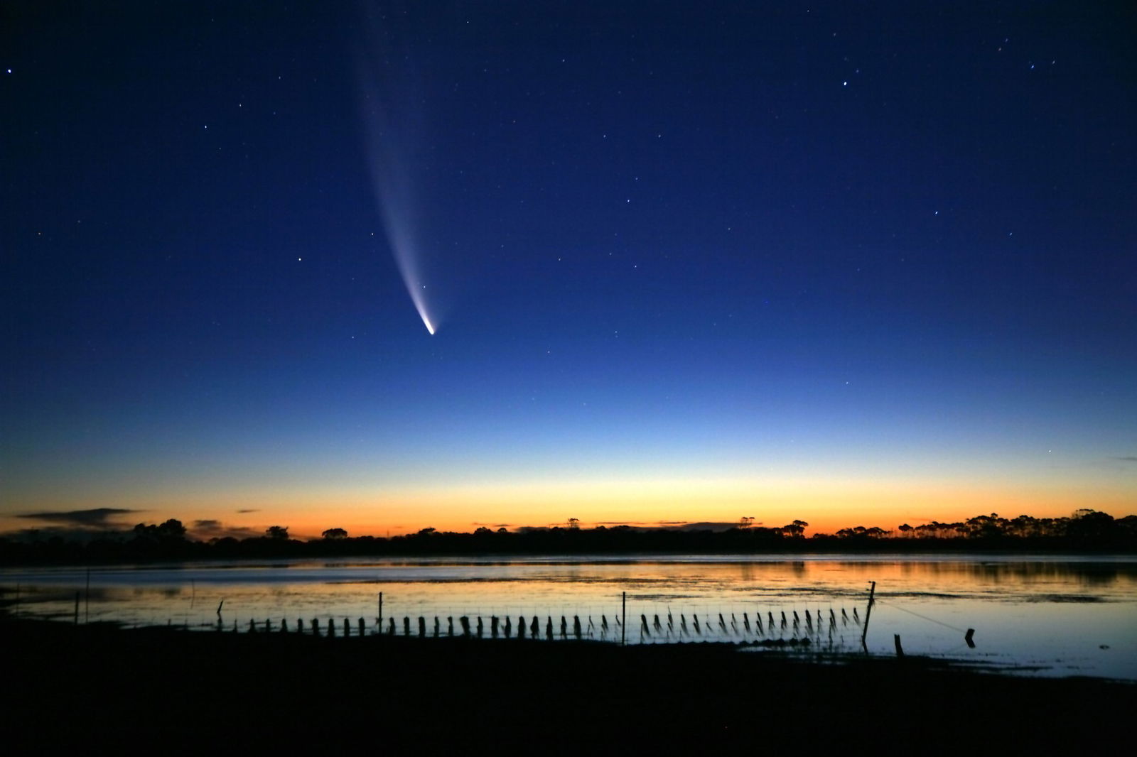 A comet flies through a sunset sky over a waterfront 