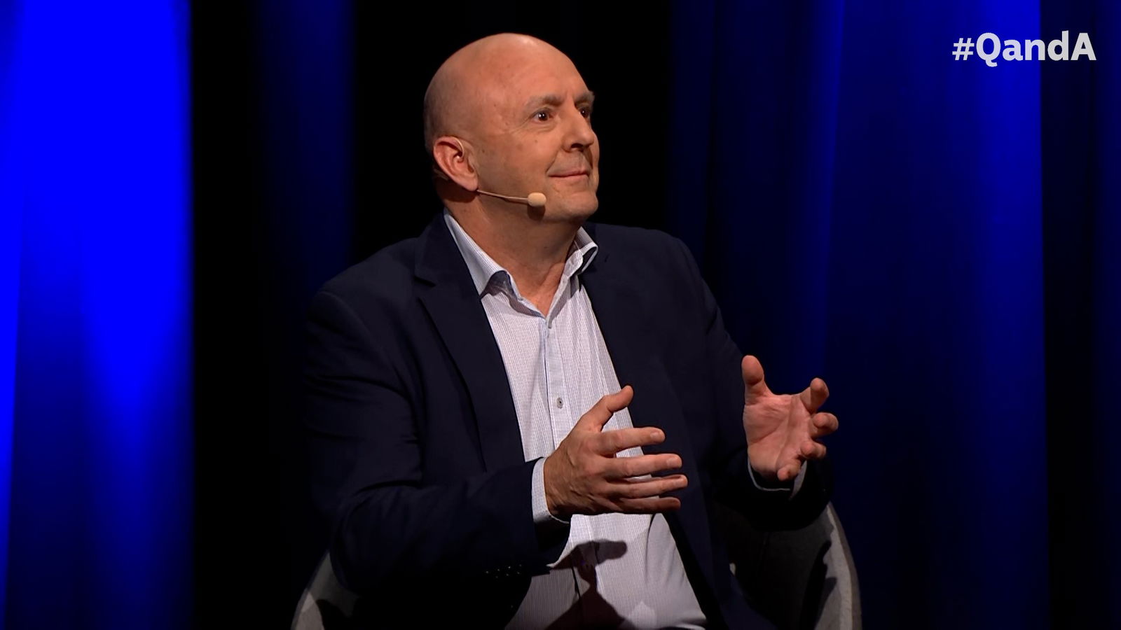 A bald man gestures with his hands.