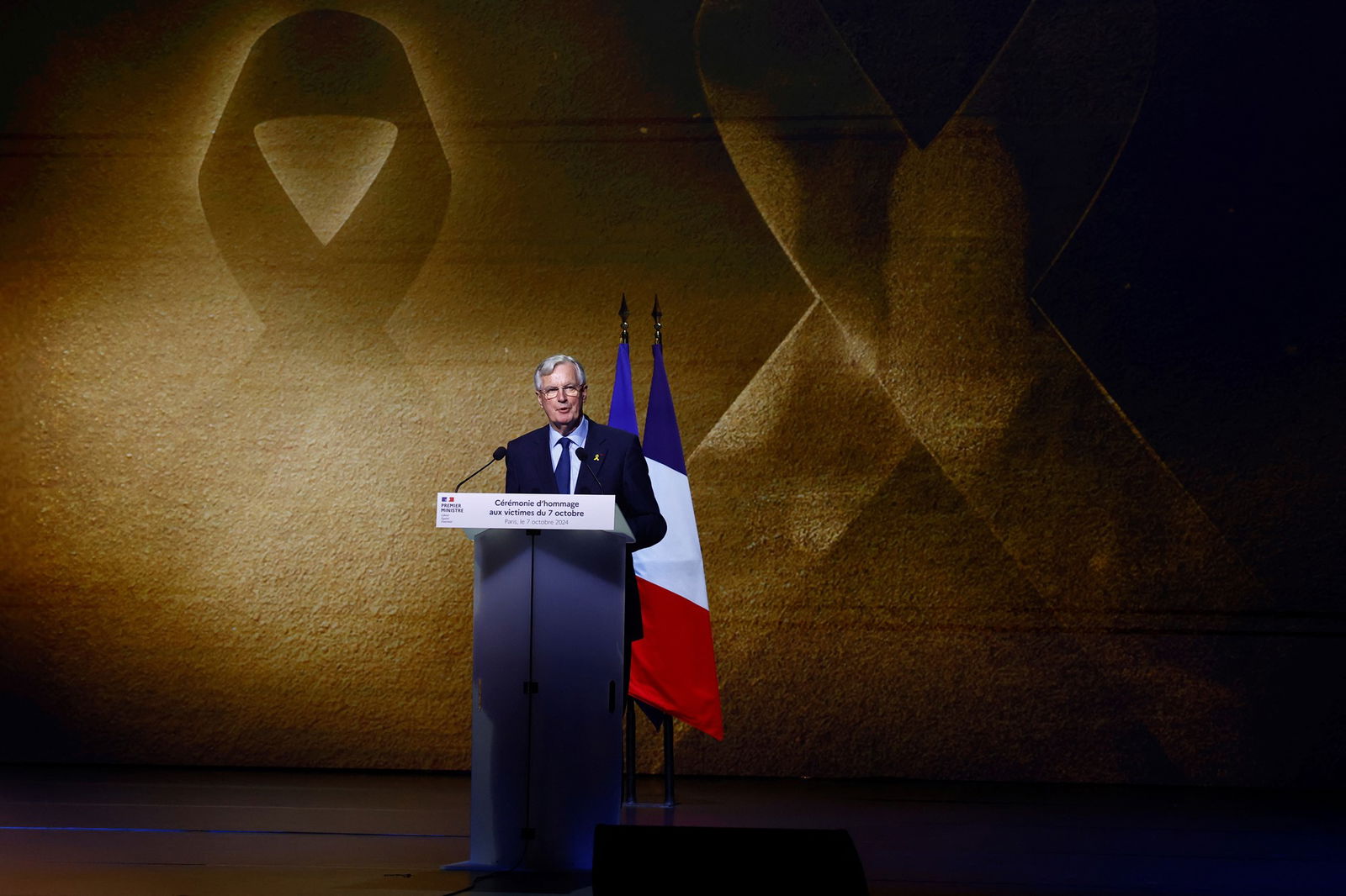 A man speaking at a lectuern in front of a French flag. 