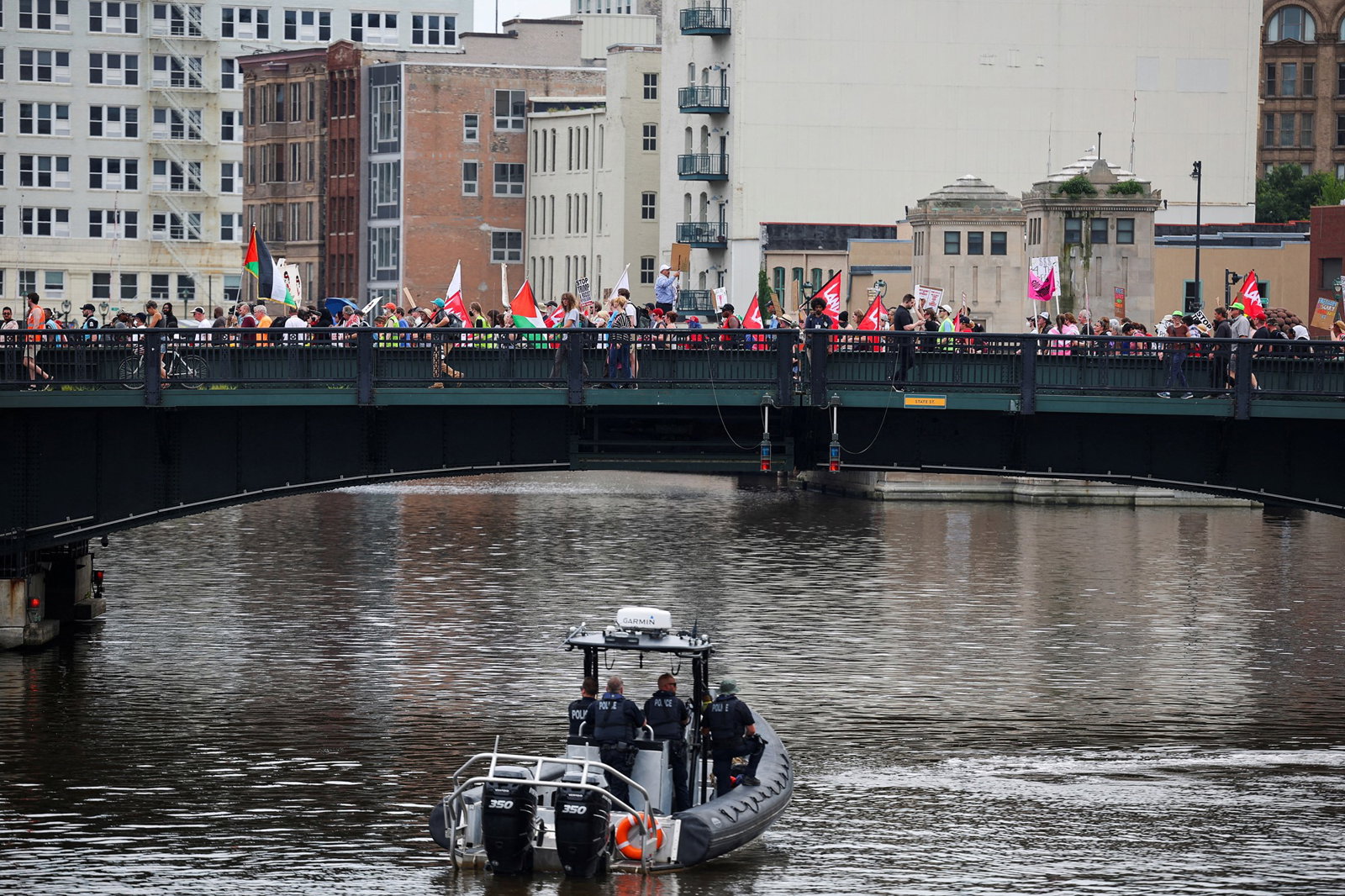 A group of protesters carrying signs and Palestinian flags walks across a bridge