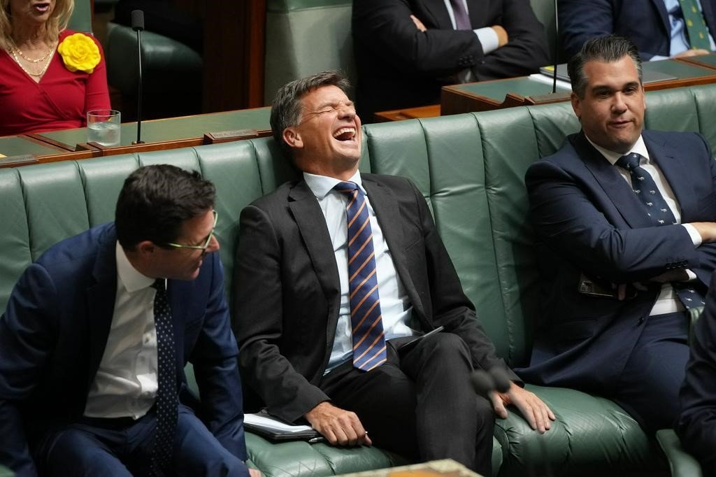 Angus Taylor sits on a bench in the House of Representatives and laughs.