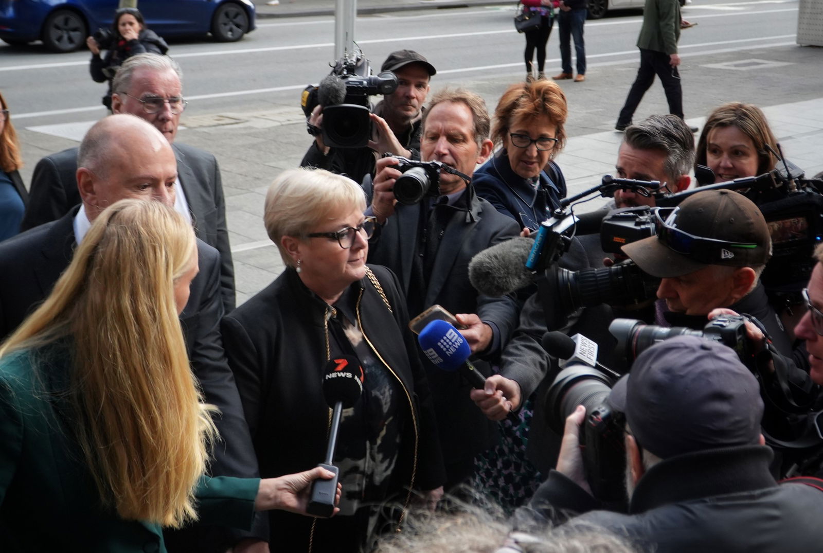 A large media scrum follows a woman into a court building