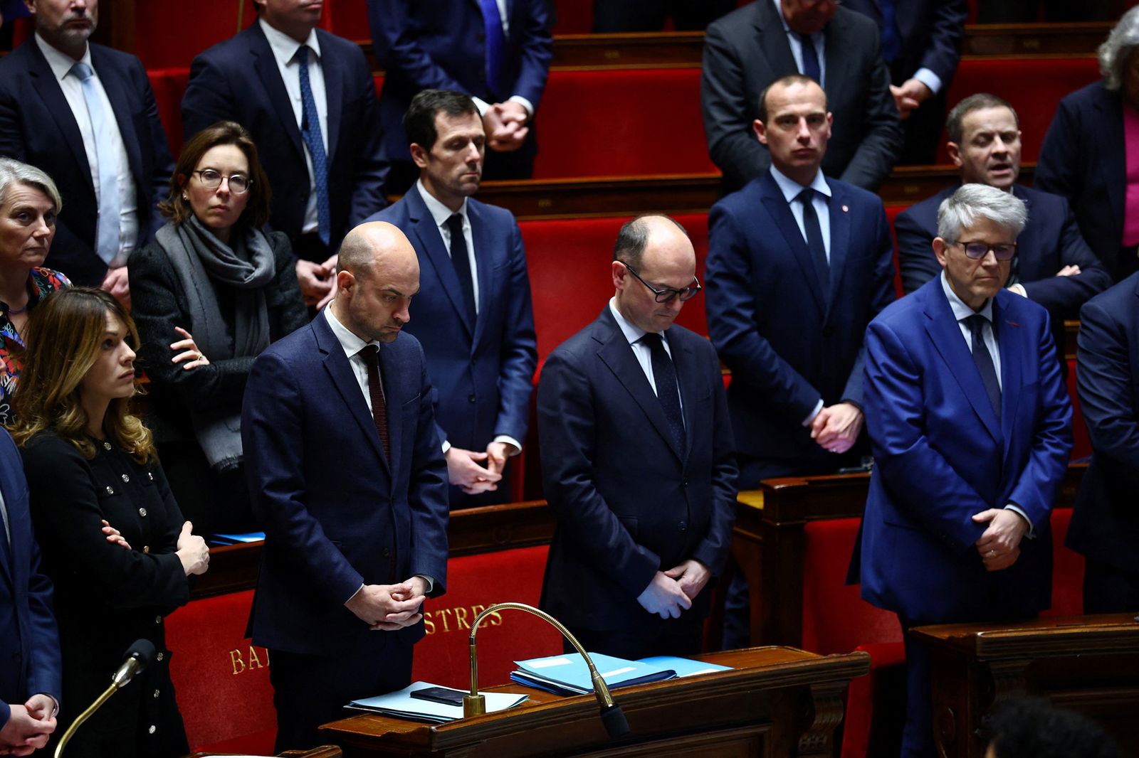 As pessoas ficam de cabeça baixa em uma sala redonda vermelha por um minuto de silêncio.