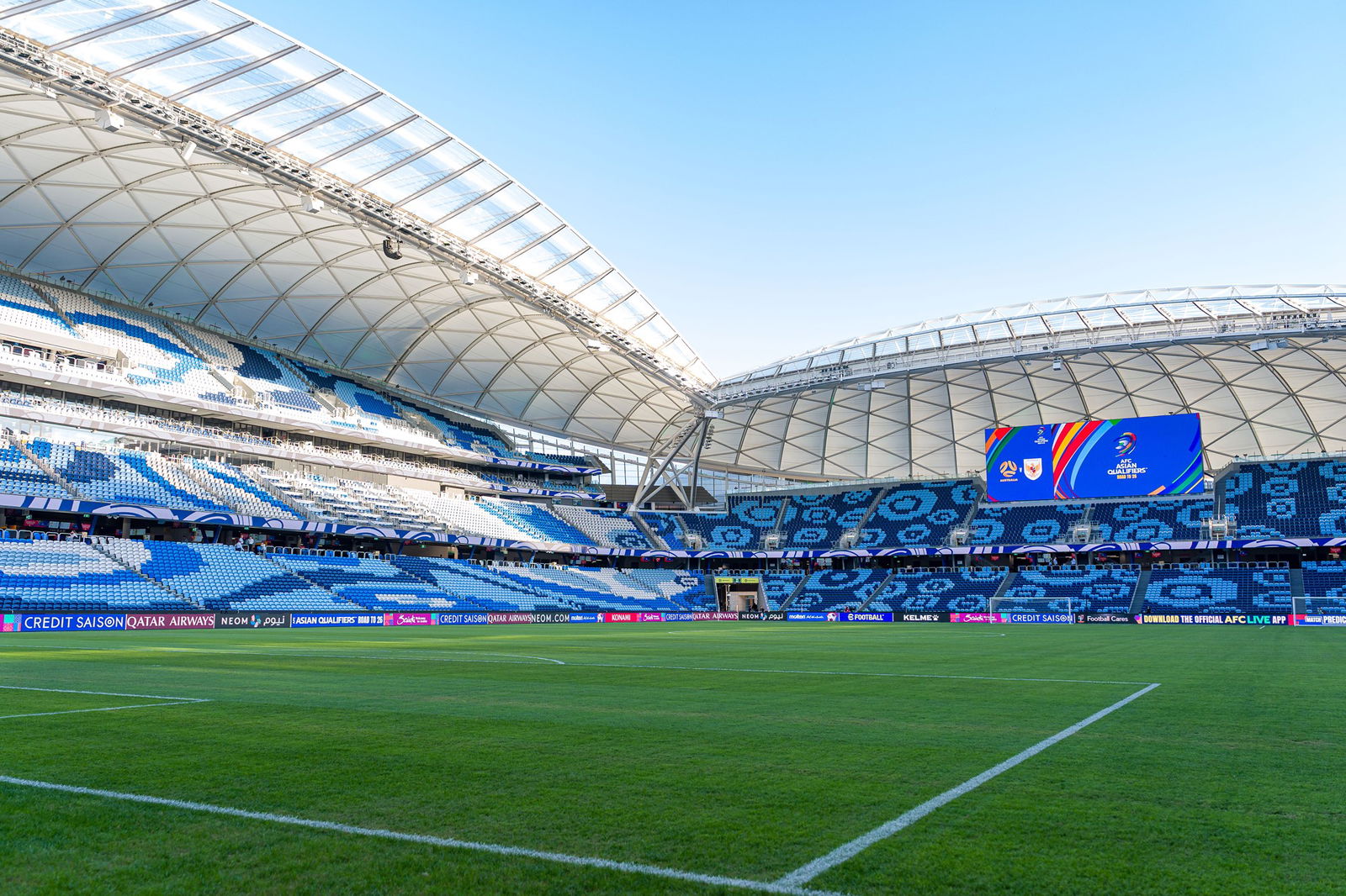 A landscape view of a sports stadium with blue seats, a green field and blue afternoon skies
