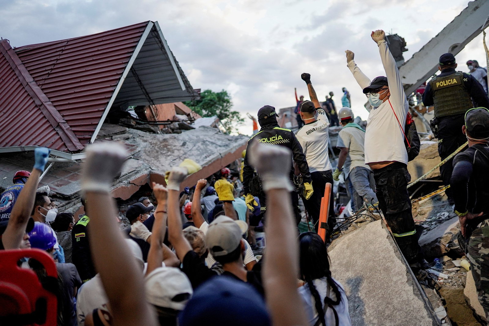 Colombians raising their fists in the air at a collapsed building.