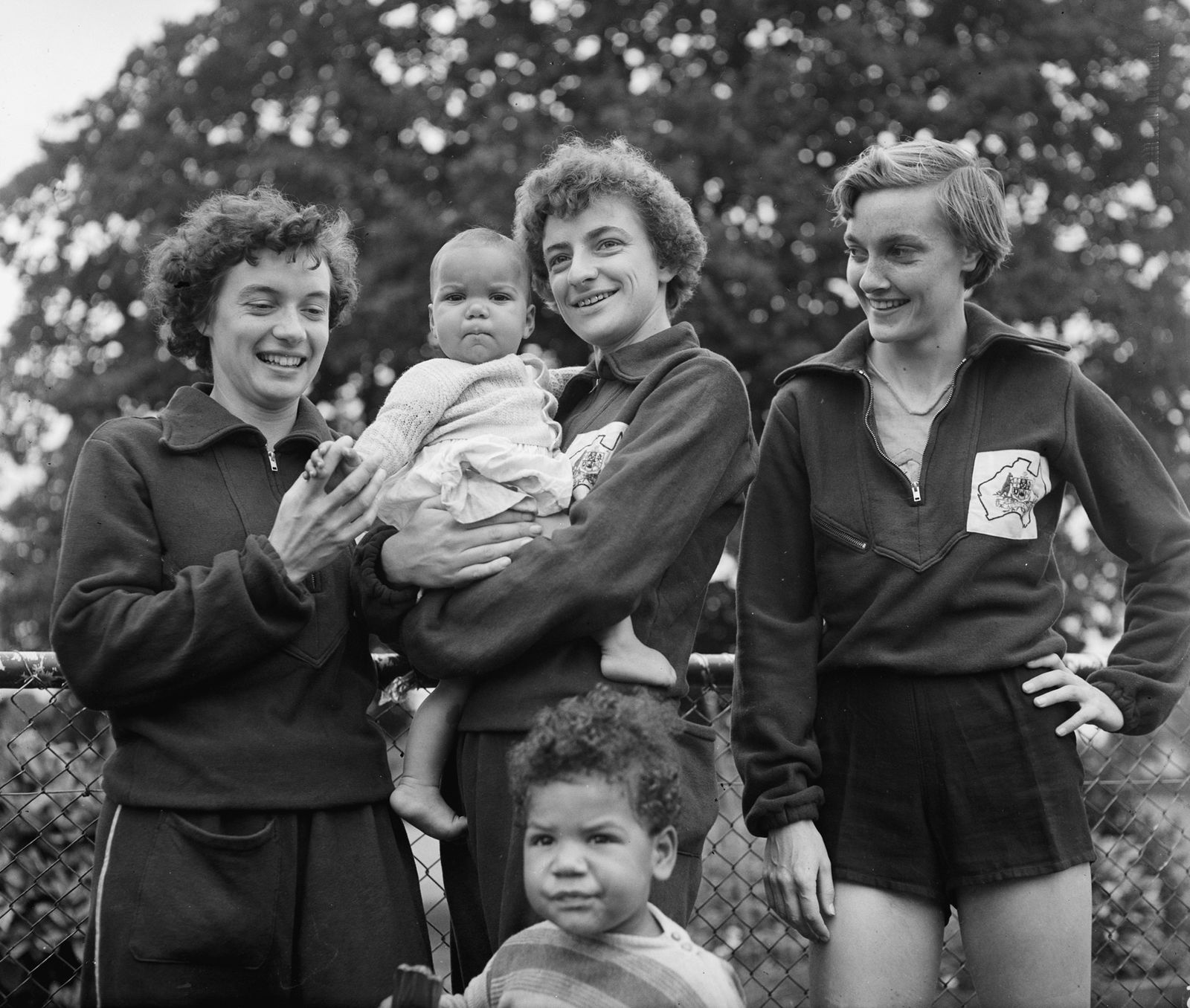 Three women stand together, middle one holding a baby.