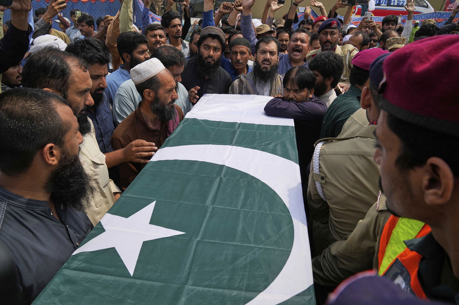 A coffin drapped in a Pakistani flag is carried through a crowd of people, some of whom are shouting