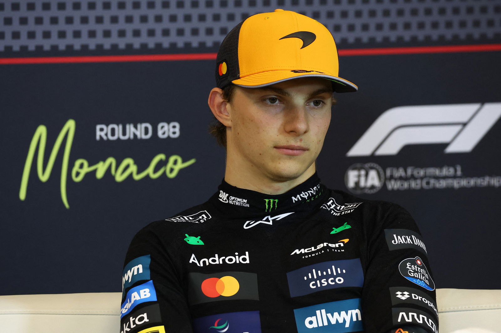 Oscar Piastri in his racing suit, sitting in a media conference