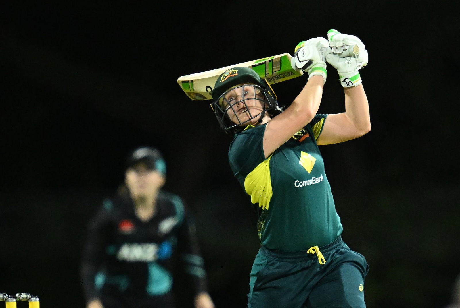 Alyssa Healy hitting a ball into the air while batting in a night match against New Zealand