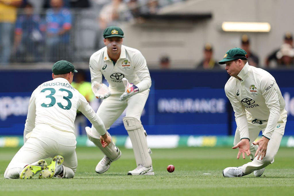 Steve Smith fields a cricket ball as Alex Carey and Marnus Labuschagne look on.