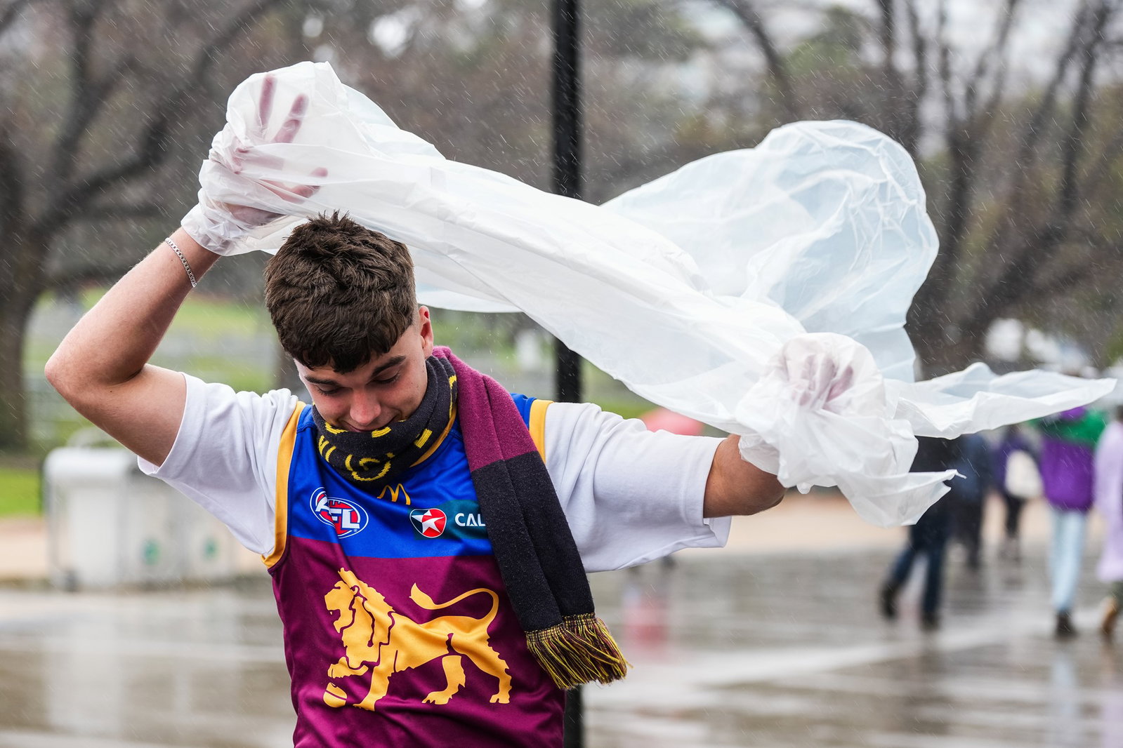 A Lions supporter attempts to put a rain jacket on while walking through the rain before the 2026 AFL Grand Final between Fremantle Dockers and Brisbane Lions at the MCG, on September 26, 2026, in Melbourne, Australia. 