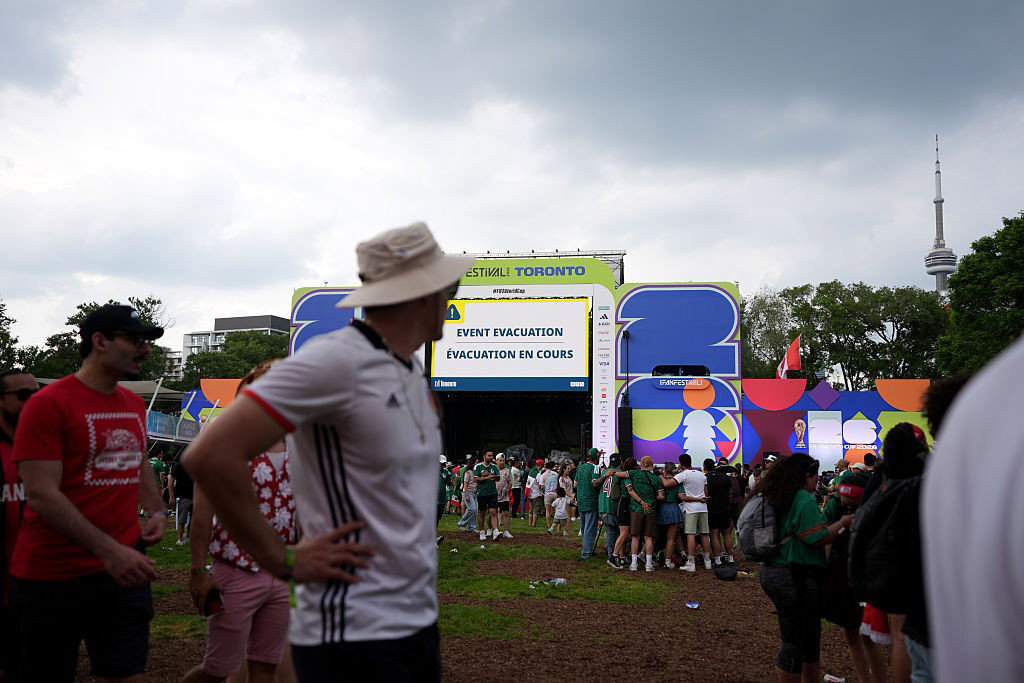 People stand in a field with a sign saying "EVENT EVACUATION"