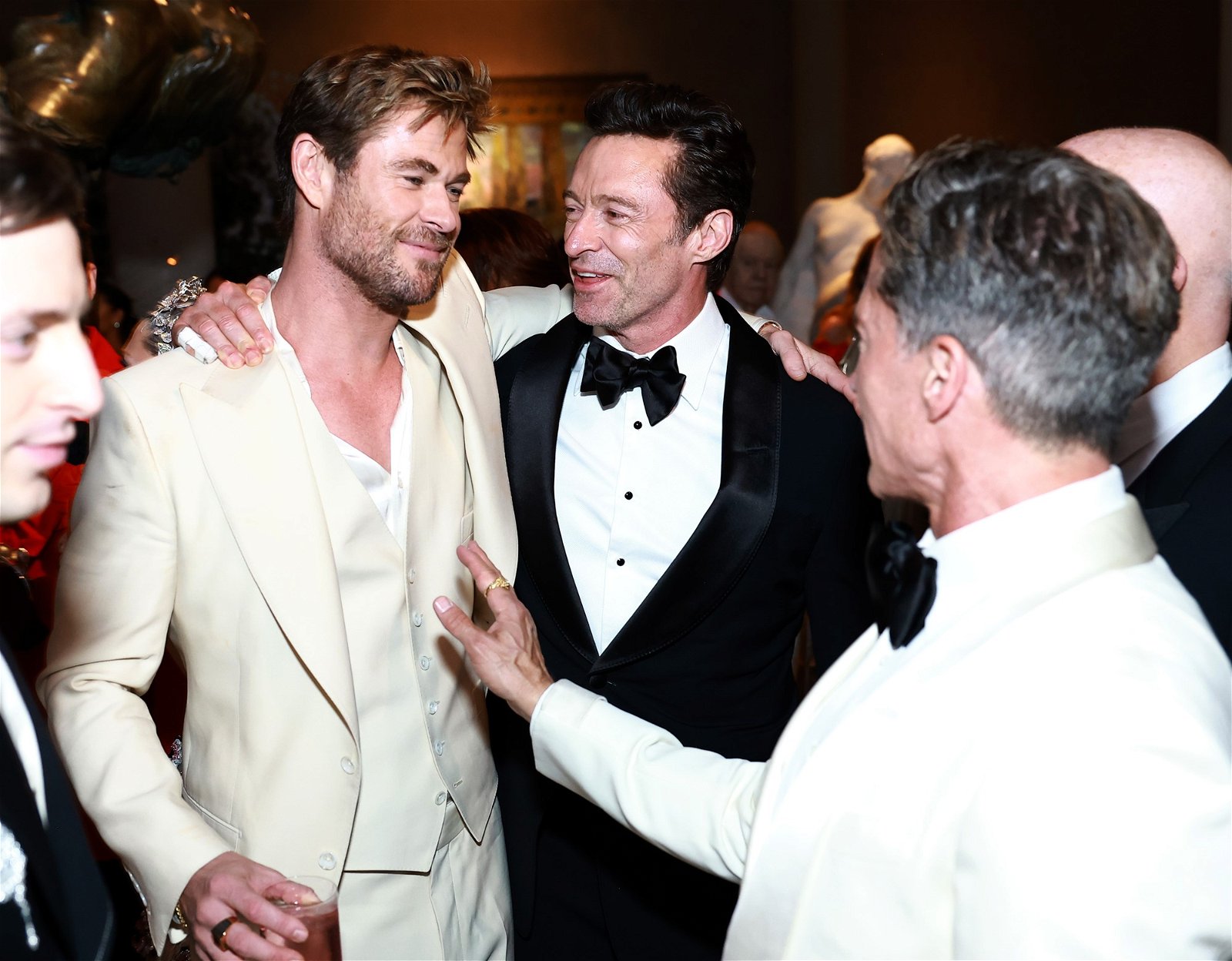 Chris and Hugh stand arm in arm as they talk with other men.