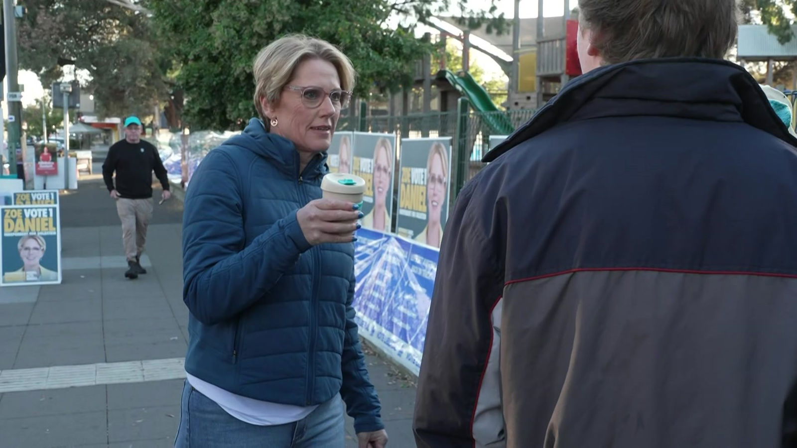 Zoe Daniels in puffer jackets holding a reusable coffee keep cup.
