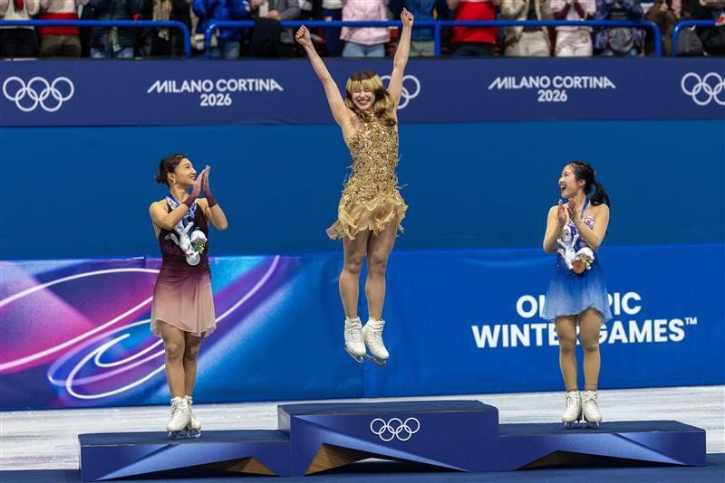 A vencedora da medalha de ouro Alysa Liu, dos Estados Unidos, sobe ao pódio para receber sua medalha, assistida pela vencedora da medalha de prata Kaori Sakamoto do Japão e pela vencedora da medalha de bronze Ami Nakai do Japão durante a Patinação Artística, Patinação Individual Feminina e Patinação Livre na Arena de Patinação no Gelo de Milão nos Jogos Olímpicos de Inverno de Milano Cortina 2026 em 19 de fevereiro de 2026 em Milão, Itália.