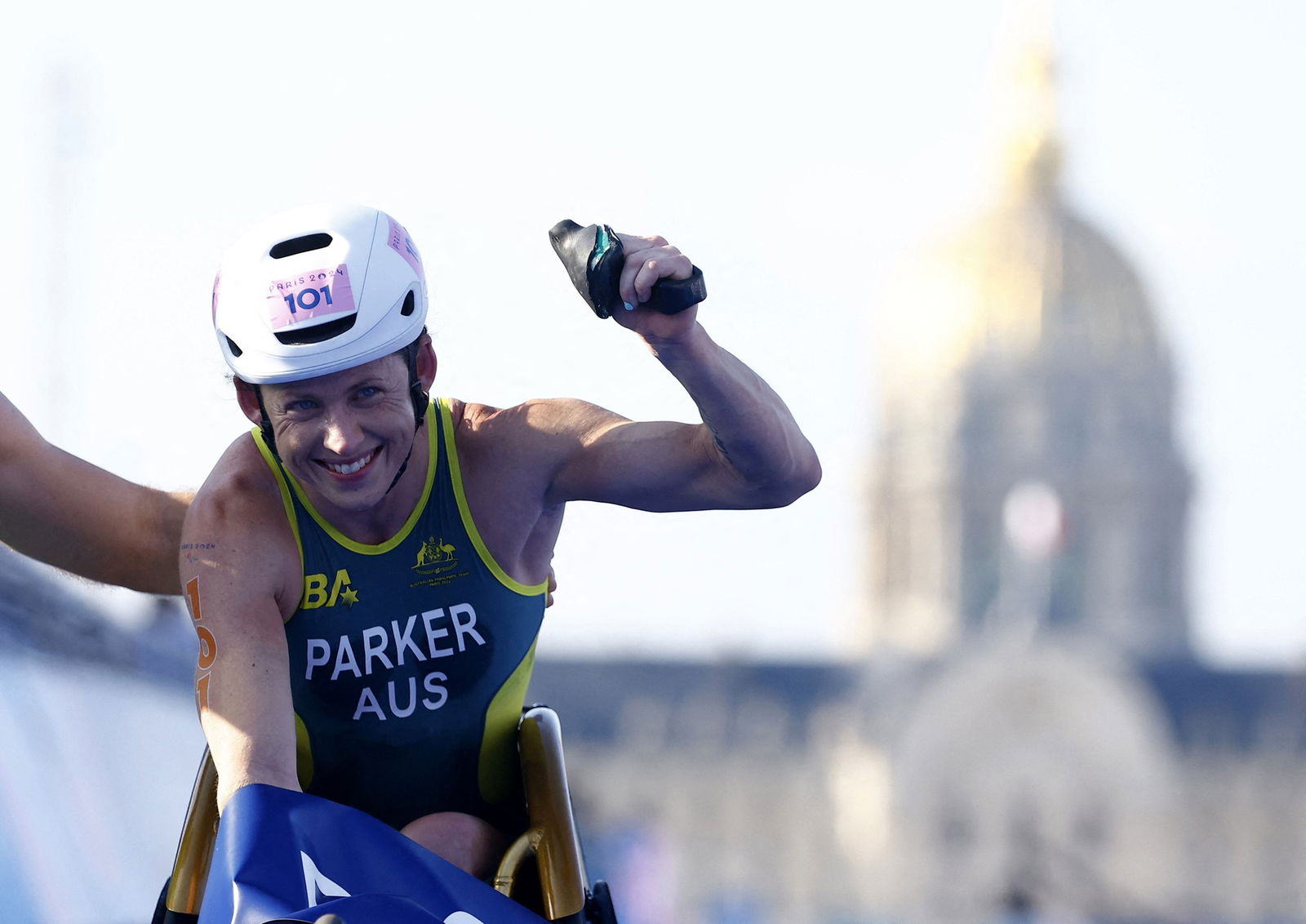 Australian Para triathlete Lauren Parker, in a racing wheelchair, pumps her fist in the air and smiles after winning gold.