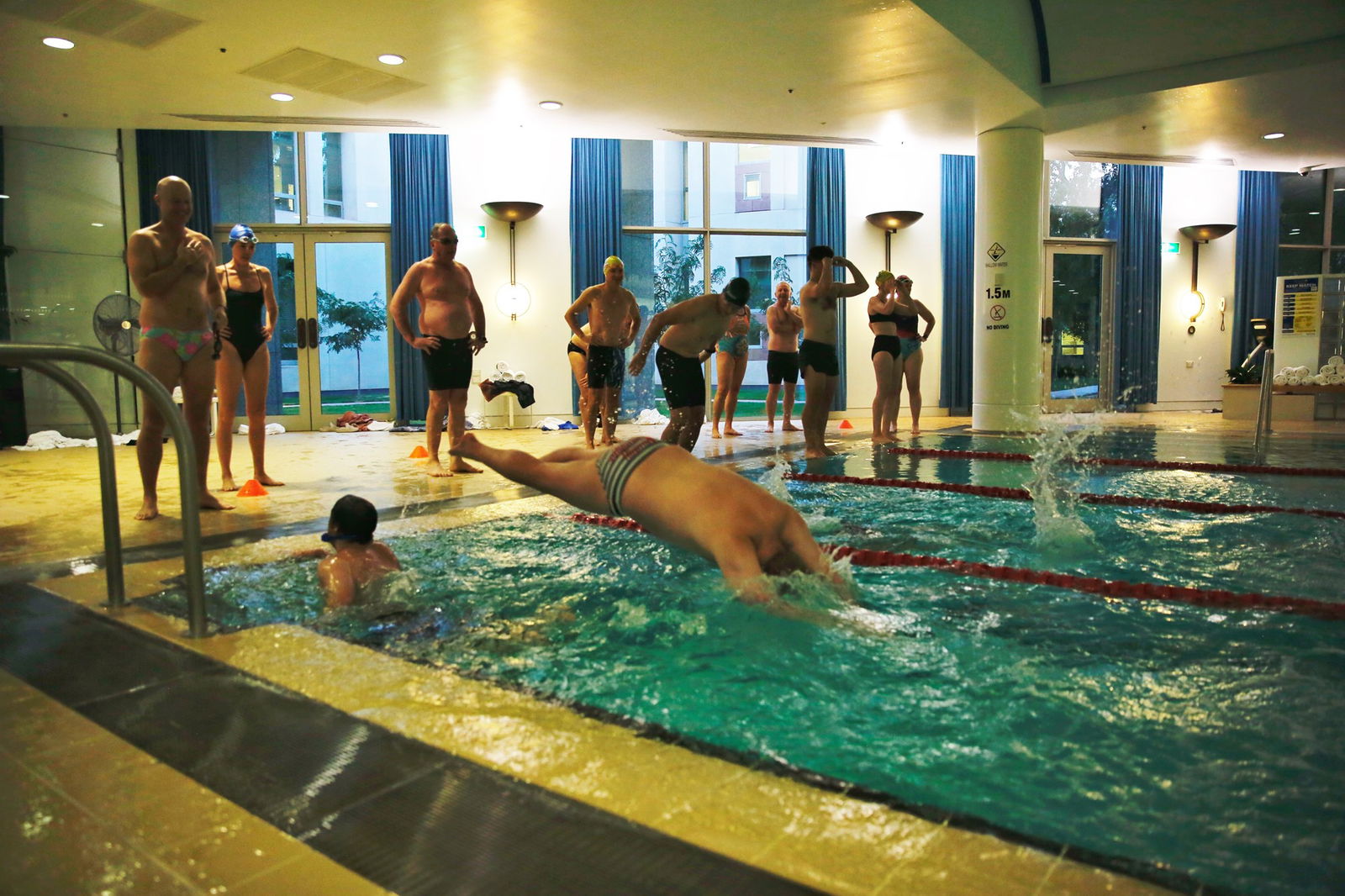 A man dives into a pool while people stand on the poolside