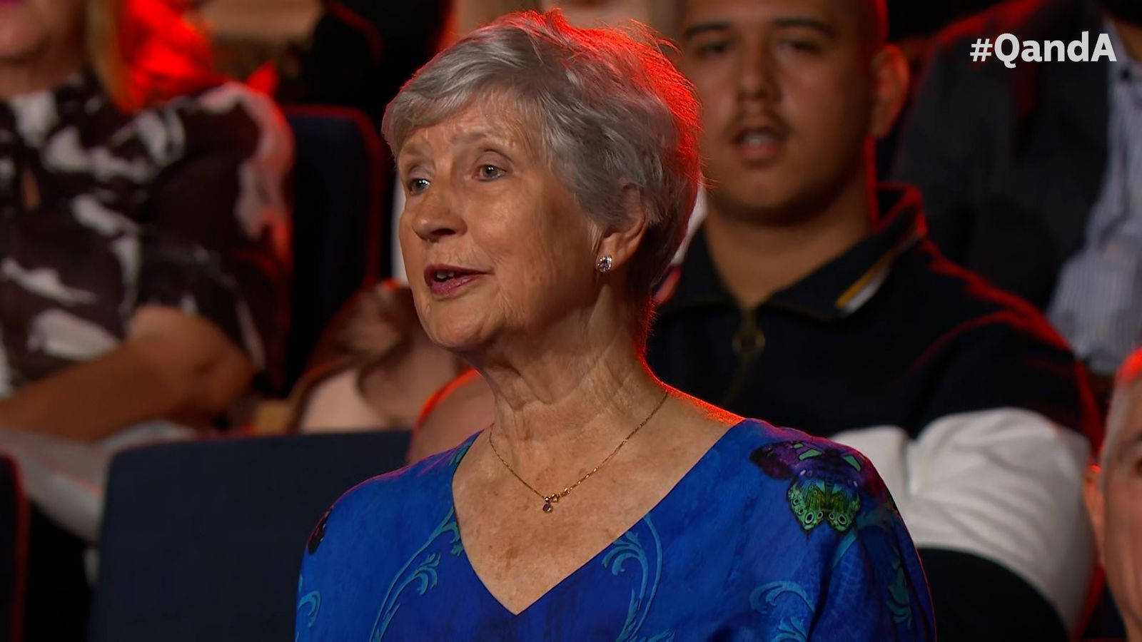 A woman in grey hair and a blue shirt speaks