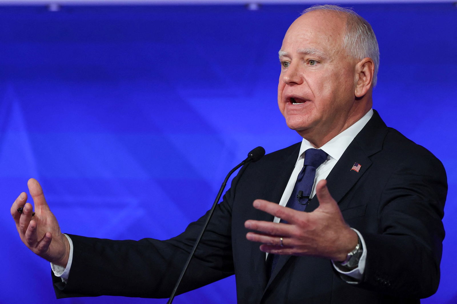 Tim Walz wearing a suit gestures with both hands