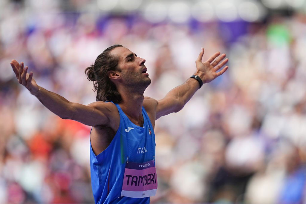 An Italian high jumper in blue raises his arms to the crowd.