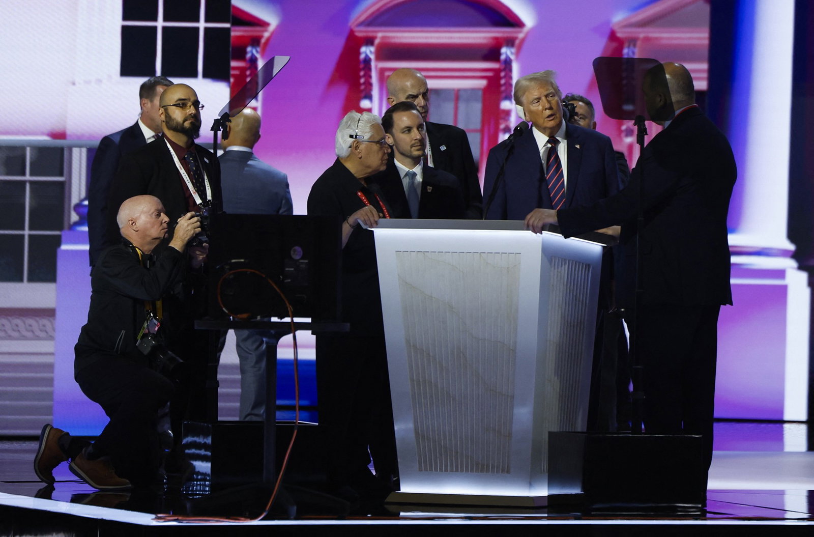 A bunch of stage hands gather around Trump on stage