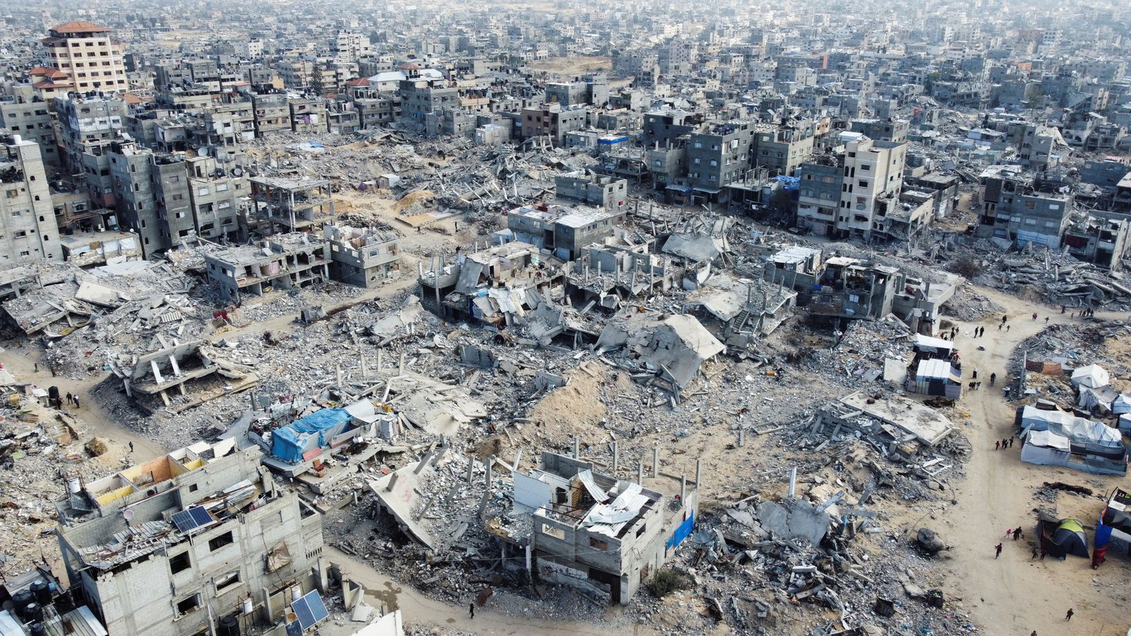 A drone view shows Palestinians walking past the rubble of houses and buildings destroyed in Israeli strikes