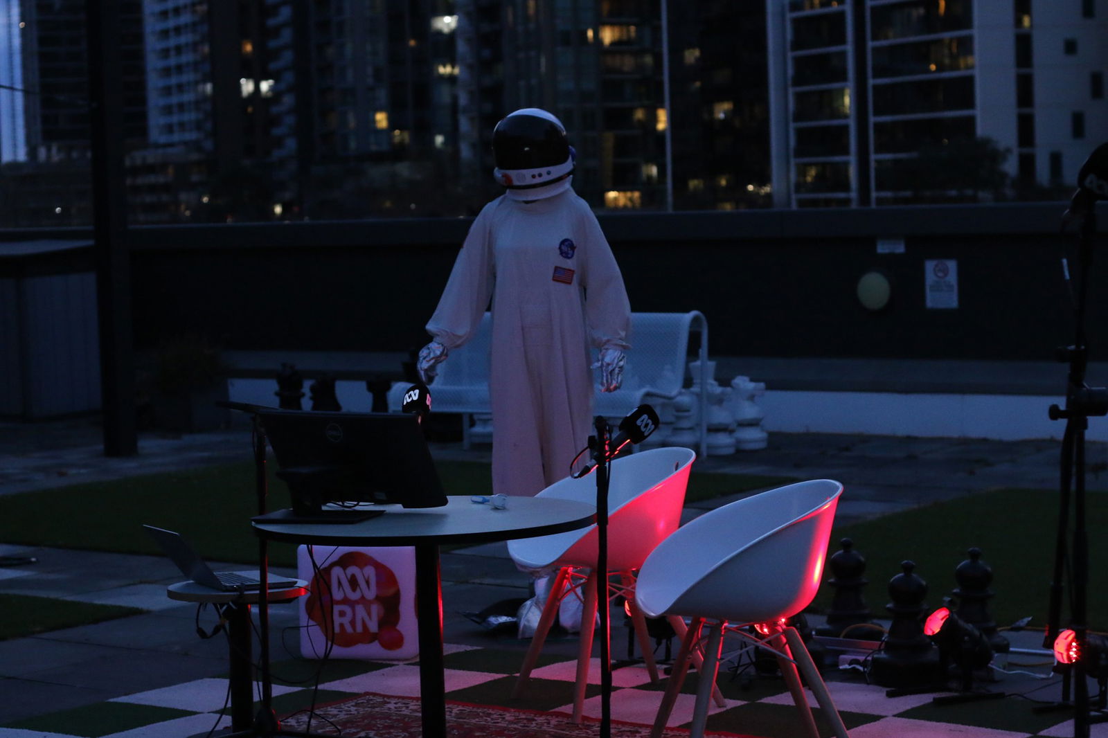 A person in an astronaut suit stands in the middle of a lawn at nig