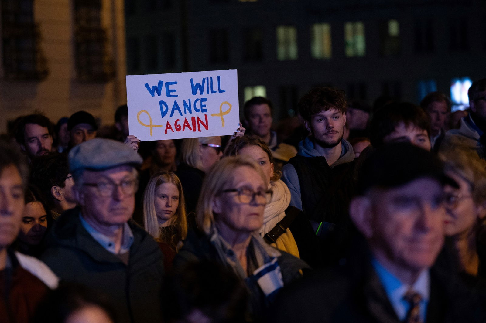 A person holds a sign which says We will dance again