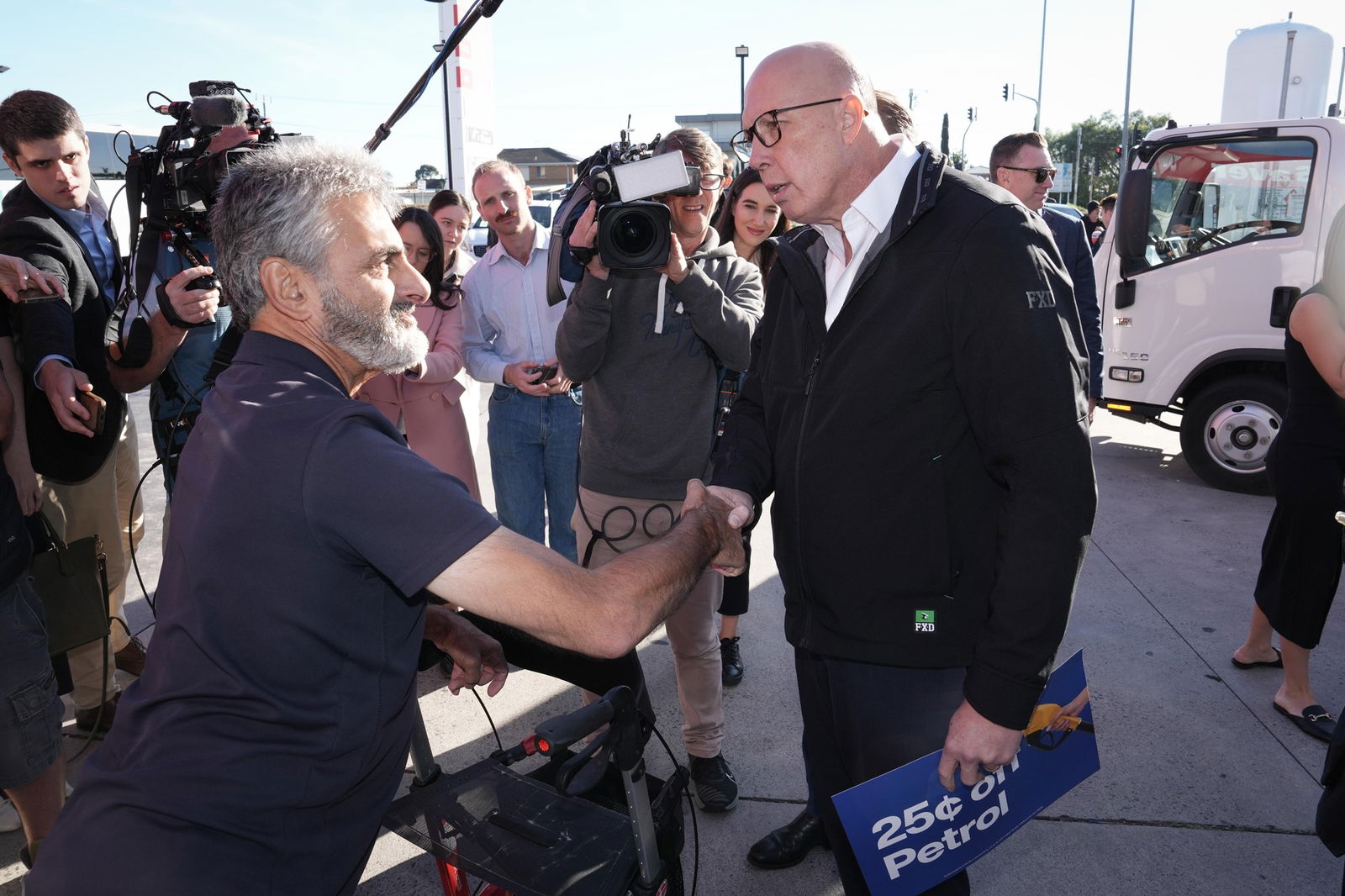 Peter Dutton shaking the hand of a man in a navy t-shirt, surrounded by TV cameras