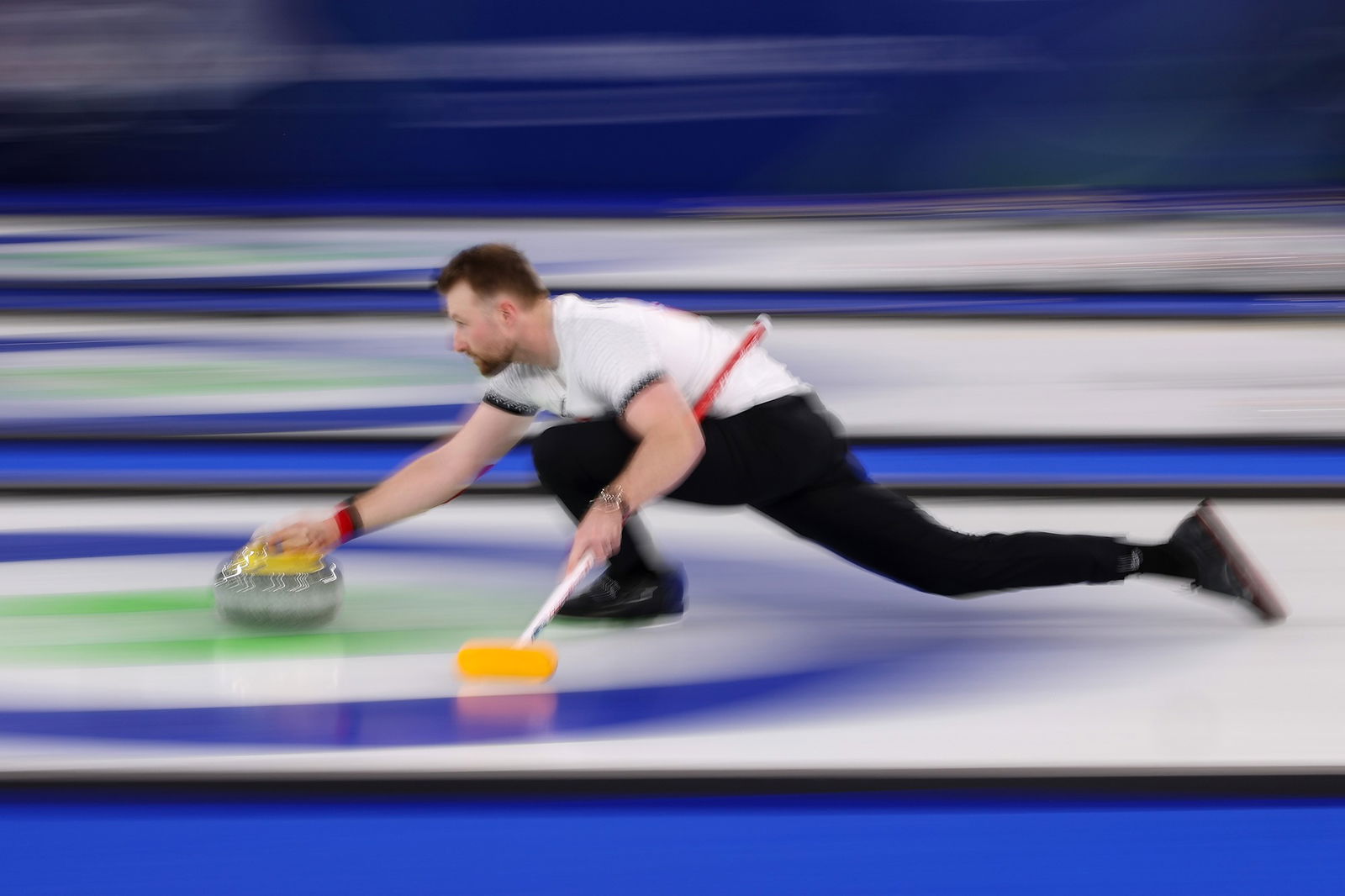 A man in white and black is crouched over while curling