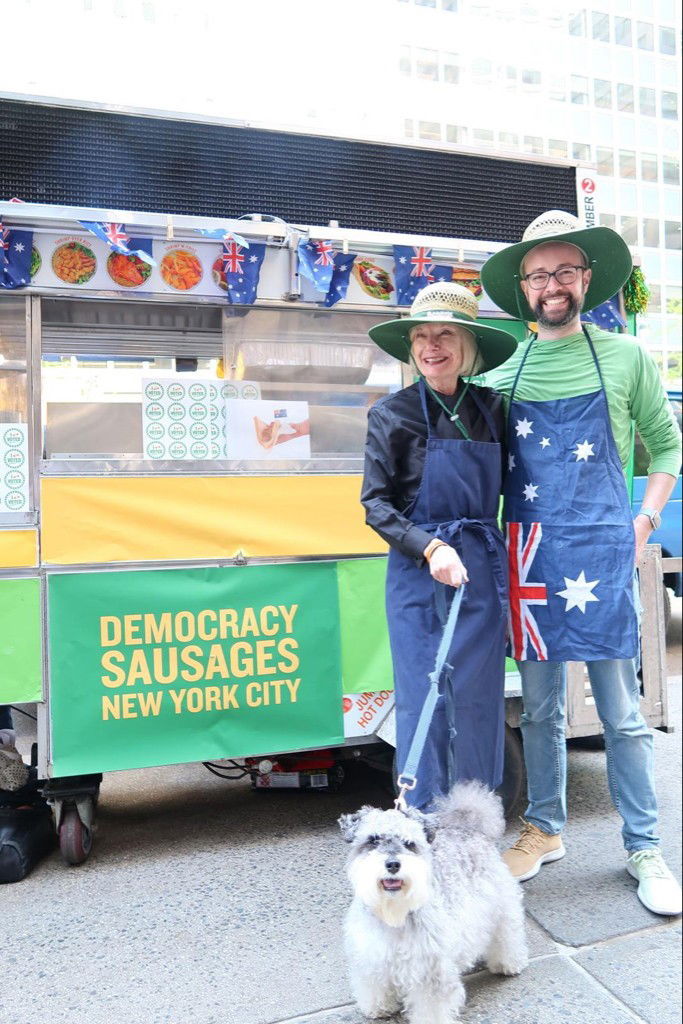 a man and woman smiling in front of a sausage sizzle food truck